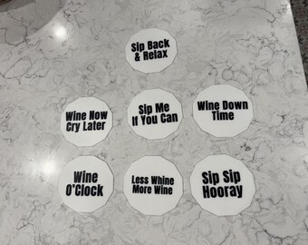May include: White, octagonal coasters with black text. Phrases include "Sip Back & Relax," "Wine Now Cry Later," "Sip Me If You Can," "Wine Down Time," "Wine O'Clock," "Less Whine More Wine," and "Sip Sip Hooray."