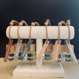 May include: A set of eight car air fresheners with wooden caps and brown string hangers. The scents are: Apple Harvest, Lemon Creme, Suede, Lodge, Ocean, Autumn Bakery.