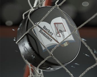 May include: A black hockey puck with a white book design. The book has the text "Hockey Romance" on the cover and a hockey stick and net illustration.
