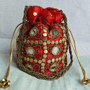 May include: A red drawstring bag with gold embellishments and mirror accents. The bag has a gold drawstring and tassel.