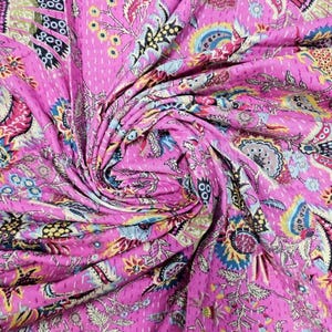 May include: A vibrant pink textile with an intricate floral and paisley pattern. The fabric is densely covered with colorful designs in shades of blue, yellow, and green. The textile is likely a quilt or a similar handcrafted item.