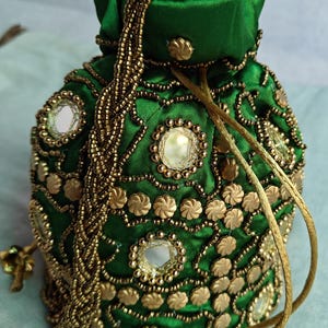 May include: A green drawstring bag with gold embellishments and mirror accents. The bag has a long gold tassel.