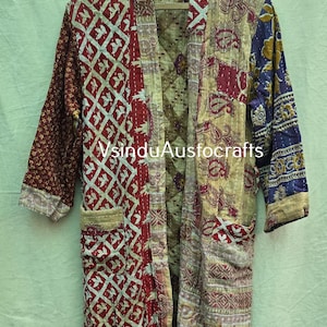May include: A patchwork robe with a variety of patterns and colors, including red, cream, and blue. The robe has pockets and is hanging on a wooden hanger. The text "sinduAustocrafts" is visible.