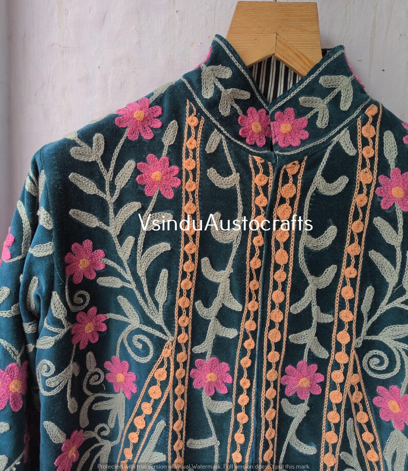 Op de afbeelding: Teal jas met ingewikkelde bloemenborduurwerk in roze, oranje en grijs. De jas heeft een hoge kraag en wordt op een houten hanger getoond. De tekst "VsinduAustocrafts" is zichtbaar.