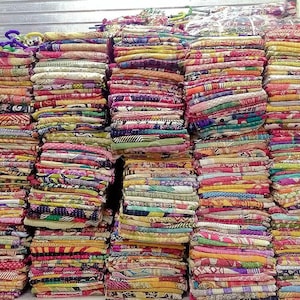 May include: A stack of colorful fabric quilts, each with a unique pattern and design. The quilts are made of various fabrics, including cotton, silk, and wool. They are arranged in a neat and organized manner, with each quilt stacked on top of the other.