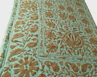 May include: A large, rectangular, light blue textile with intricate brown floral embroidery. The design features stylized flowers, leaves, and paisley motifs, creating a detailed and textured pattern across the surface.