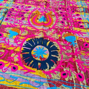 Op de afbeelding: Een kleurrijk kantha-deken met een bloemenpatroon in tinten roze, blauw, geel en oranje. Het deken is gemaakt van gerecyclede sari's en heeft een uniek, handgestikt ontwerp.