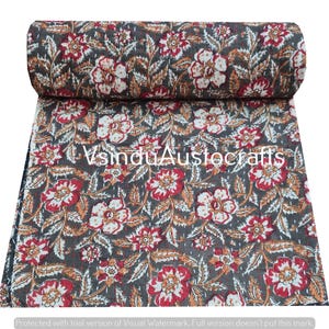 May include: A rolled-up, floral-patterned quilt with a dark gray background. The quilt features a repeating pattern of red and white flowers with orange accents and green leaves. The text "VsinduAustocrafts" is visible on the quilt.