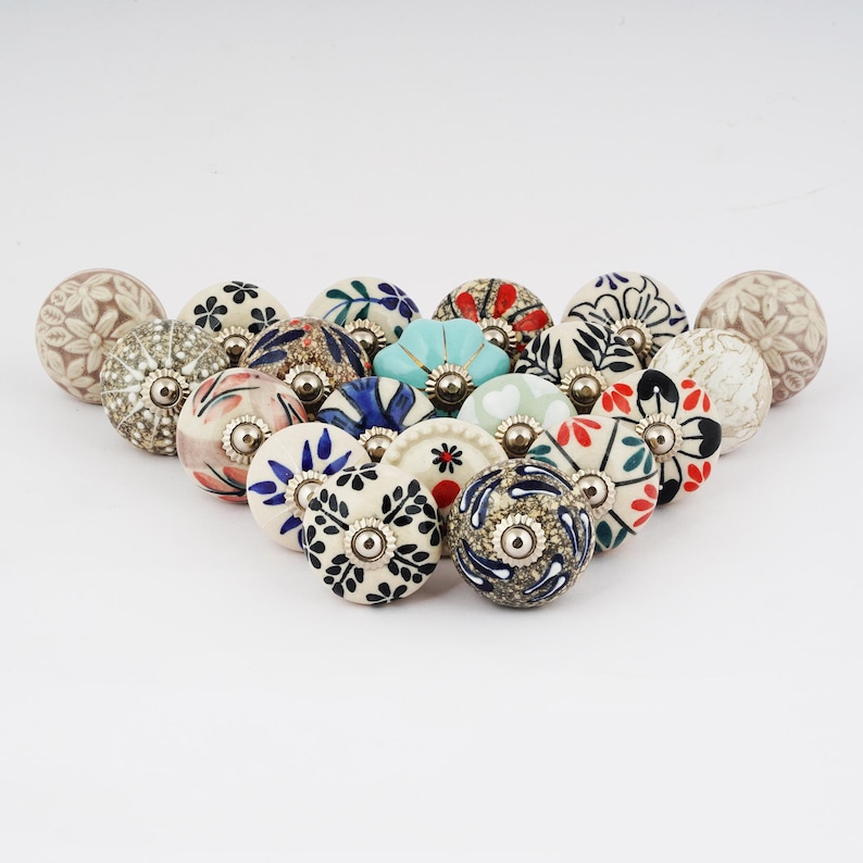 Op de afbeelding: Een verzameling van 16 keramische ladeknopjes met verschillende bloem- en geometrische patronen in tinten blauw, rood, groen, wit en goud. De knopjes zijn ongeveer 2,5 cm in diameter.