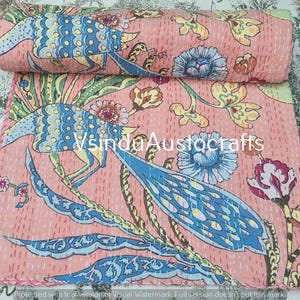 May include: A peach-colored cotton quilt featuring a repeating pattern of blue and yellow birds alongside floral motifs in shades of blue, yellow, and green. The fabric is finished with white running stitch quilting and displays the text VsinduAustocrafts.