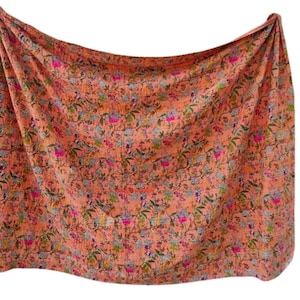 May include: A peach-colored textile with a floral pattern. The design features small flowers in shades of pink, blue, and green, scattered across the fabric. The textile is draped, showcasing its texture and the intricate details of the print.