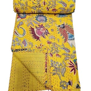 May include: A rolled-up yellow quilt with a floral pattern in shades of pink, blue, and green. The quilt is made of a soft material and has a stitched design. The quilt is a decorative home textile.