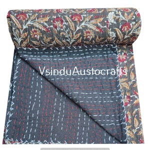 May include: A rolled-up, dark gray quilt with a floral pattern in red, white, and gold. The quilt is partially unfolded, revealing a dark gray interior with white and red stitching. The text "VsinduAustocrafts" is visible.