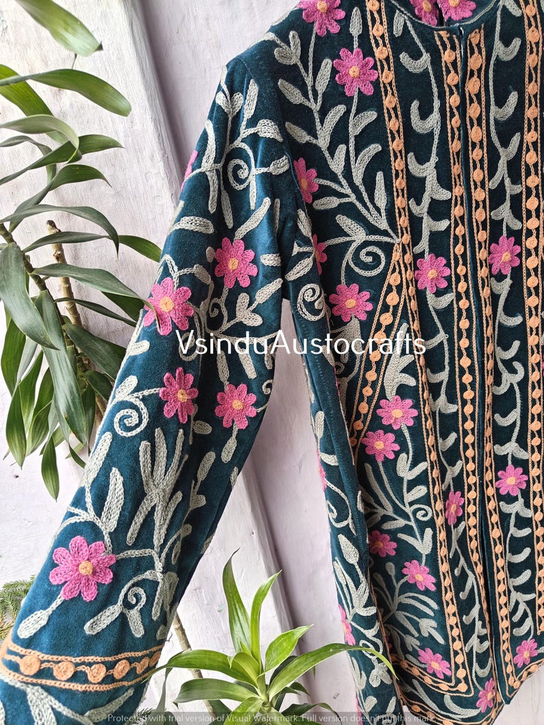 Op de afbeelding: Teal jas met ingewikkelde bloemenborduurwerk in roze en lichtbeige. De jas heeft een hoge kraag en lange mouwen, met de tekst "VsinduAustocrafts" zichtbaar. Het borduurwerk omvat bloemen en wervelende bladerpatronen.