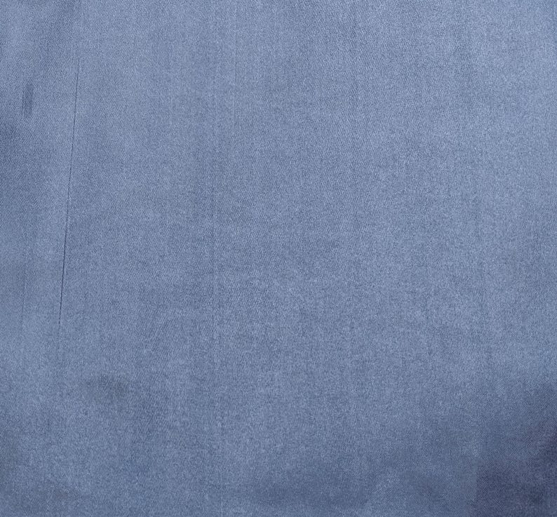 Puede incluir: Primer plano de una tela texturizada en un tono azul gris&aacute;ceo apagado. El material tiene una superficie sutil, ligeramente irregular, con l&iacute;neas verticales y peque&ntilde;as imperfecciones. El aspecto general es suave y mate.