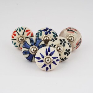 Op de afbeelding: Zes keramische knoppen met verschillende bloemenpatronen in tinten blauw, groen, rood en roze. Elke knop heeft een zilveren metalen basis.