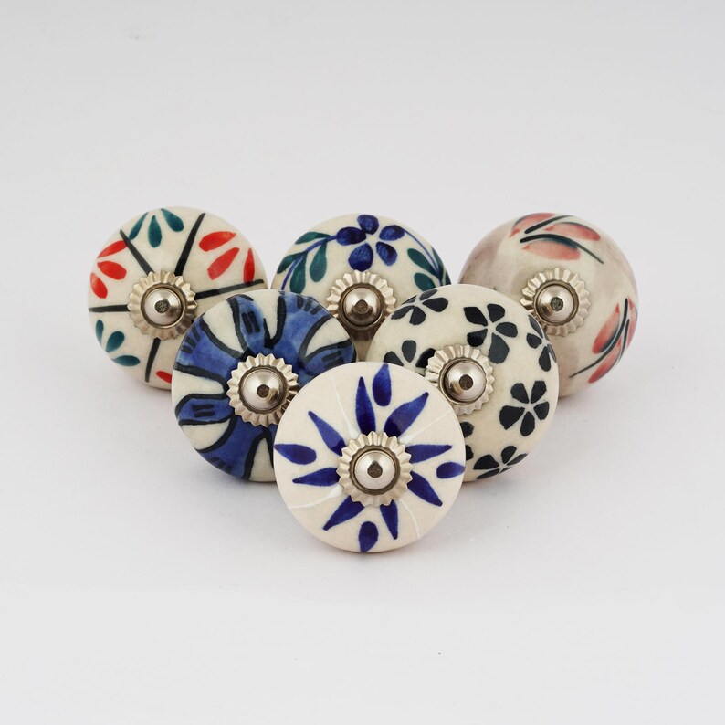 Op de afbeelding: Zes keramische knoppen met verschillende bloemenpatronen in tinten blauw, groen, rood en roze. Elke knop heeft een zilveren metalen basis.