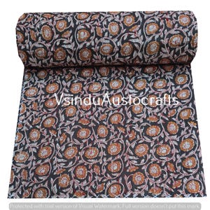 May include: Rolled fabric with a repeating floral pattern. The design features orange and white flowers with green vines on a dark background. The text "VsinduAustocrafts" is visible. The fabric is likely used for sewing or crafting projects.