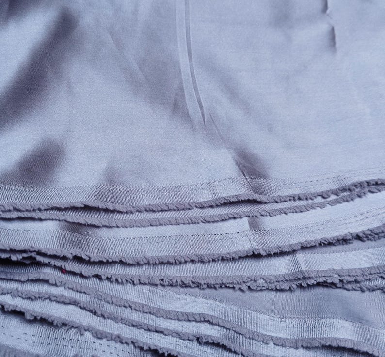 Puede incluir: Primer plano de una pila de tela azul claro con bordes deshilachados. La tela parece ser un material suave y tejido, posiblemente algod&oacute;n o lino. Las capas est&aacute;n cuidadosamente apiladas, mostrando la textura y las variaciones de color.