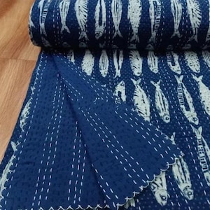 May include: A rolled-up navy blue and white quilt with a fish pattern. The quilt is made of a soft fabric and features a repeating design of white fish on a dark blue background. The edges are scalloped and stitched with white thread.
