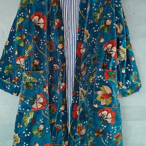 Puede incluir: Una bata de terciopelo azul turquesa con estampado floral. La bata tiene un forro a rayas y dos bolsillos.