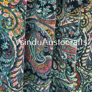 Peut inclure: Gros plan sur un tissu avec un motif cachemire vibrant dans les tons de turquoise, rose, orange et vert sur fond noir. Le texte "VsinduAustocrafts" est visible. Le tissu est probablement utilisé pour les vêtements ou la décoration intérieure.