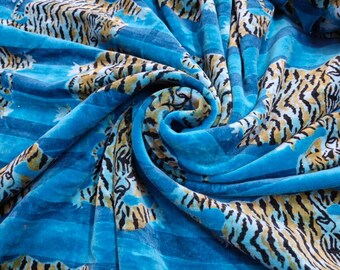 May include: Blue fabric with a repeating pattern of black and orange tigers. The fabric is folded and textured.