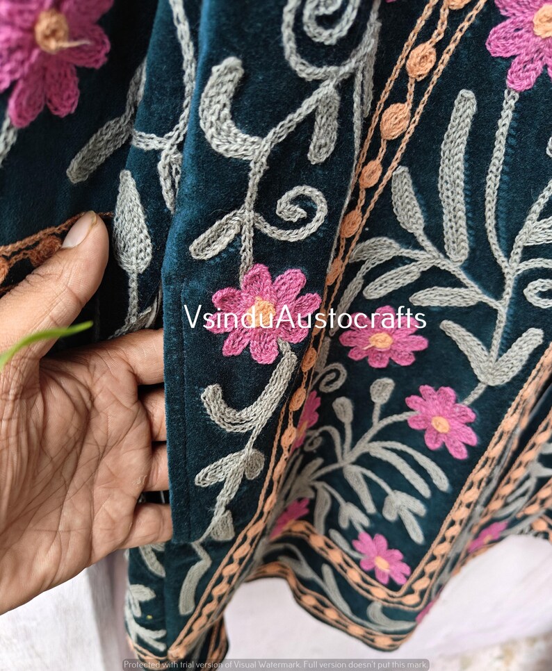 Op de afbeelding: Close-up van een teal stof met ingewikkelde bloemenborduurwerk. Roze bloemen en grijze ranken zijn op de stof gestikt, met een rand van oranje en bruin borduurwerk. De tekst "VsinduAustocrafts" is zichtbaar.