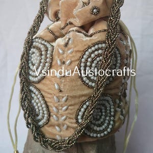 Può includere: Una borsa a coulisse in velluto beige con intricate perline. La borsa presenta un manico intrecciato ed è adornata con perline bianche e dorate a spirale e a goccia. Il testo "VsinduAustocrafts" è visibile sulla borsa.