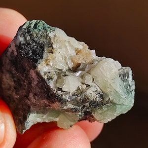 May include: A close-up of a green and white crystal cluster with a rough, dark gray exterior. The crystal cluster has a natural, raw appearance.
