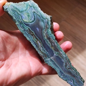 Può includere: Una lastra di agata verde e grigia con un motivo a spirale. L'agata ha una superficie liscia e lucida.