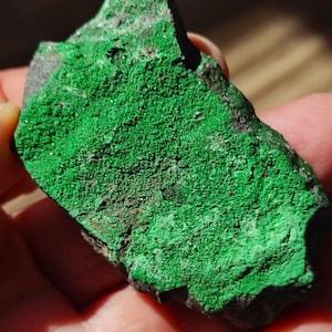 May include: A rough, dark gray rock with a bright green mineral coating. The green mineral appears to be a crystalline formation.