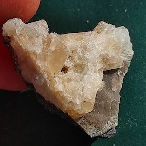 May include: A cluster of small, translucent, light brown crystals on a dark gray rock. The crystals have a rough, textured surface.