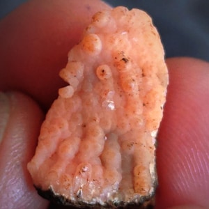 May include: A close-up of a pink and white agate geode with a rough, textured surface. The geode has a cluster of small, rounded crystals.