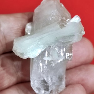 Op de afbeelding: Een cluster van heldere kwartskristallen met een lichtgroen aquamarijnkristal erop. De kristallen zijn doorschijnend en hebben een natuurlijke, ruwe textuur.