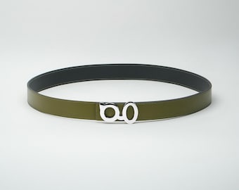 May include: Olive green belt with a silver-tone buckle. The belt has a black interior and a silver buckle with a unique design. The belt is made of a smooth material and is suitable for various outfits.