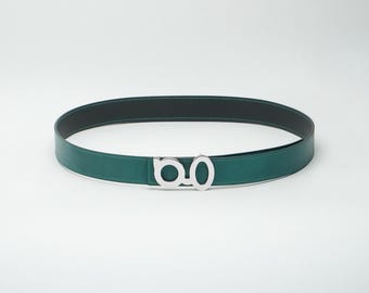 May include: A green leather belt with a silver-colored buckle. The belt has a black interior and white stitching. The buckle is a stylized double-O design. The belt is approximately 1.25 inches wide.