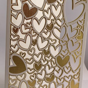 May include: A white card with a gold background and a cut-out design of many hearts. The hearts are layered and overlap, creating a complex and intricate pattern.