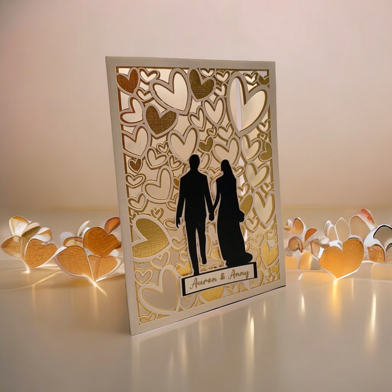 May include: A white card with a gold heart design and a silhouette of a couple holding hands. The card says "Aaron & Amy" at the bottom.