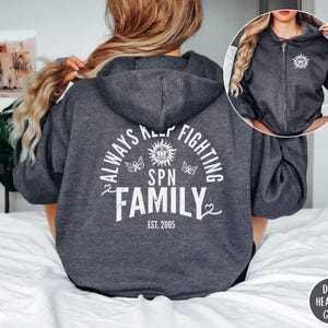 May include: Dark heather grey zip-up hoodie with white text that reads "ALWAYS KEEP FIGHTING SPN FAMILY EST. 2005" and a sun and butterfly graphic. A smaller image shows the front of the hoodie with a sun graphic.