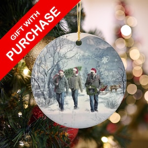 May include: Round Christmas ornament featuring three people walking in a snowy forest, wearing Santa hats. The ornament has the words "Merry Christmas" and "Happy New Year!" on it. A red banner reads "GIFT WITH PURCHASE".