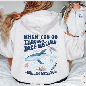 Könnte beinhalten: Ein hellgrauer Kapuzenpullover mit einem Grafikdruck eines Wals, eines Seesterns und einer Meeresschildkröte. Der Text auf dem Pullover lautet "When you go through deep waters I will be with you" und "Isaiah 43:2".
