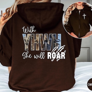 Könnte beinhalten: Schokoladenbrauner Kapuzenpullover mit Reißverschluss und dem Text "With YHWH She will ROAR" sowie einer Löwengrafik. Der Hoodie hat eine Kapuze und ein weißes Kreuz auf der Brust. Die Farbe ist als "Chocolate" angegeben.