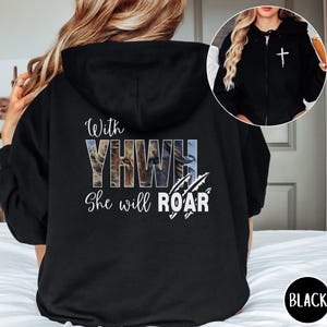 Könnte beinhalten: Schwarzer Kapuzenpullover mit Reißverschluss und dem Text "With YHWH She will ROAR" in Weiß sowie einer Löwengrafik. Der Hoodie hat eine Kapuze und ein weißes Kreuz auf der Brust. Das Wort "BLACK" befindet sich in einem schwarzen Kreis.