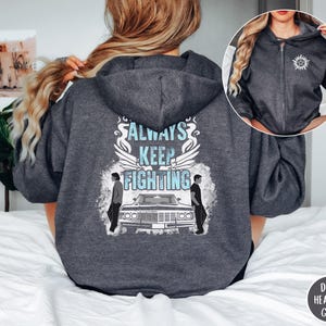 May include: Dark heather grey zip-up hoodie with a graphic on the back that says "ALWAYS KEEP FIGHTING" with a car and two figures. A smaller image of the hoodie is in the upper right corner. The hoodie has a hood and a zipper.