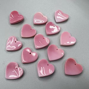 Puede incluir: Una colecci&oacute;n de 13 dijes de concha de coraz&oacute;n rosa con un agujero en la parte superior para colgar.