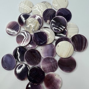 May include: A collection of round, purple and white shell pendants with a hole drilled through the top. The shells have a natural, striated pattern.