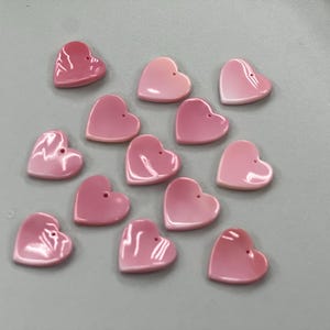 Puede incluir: Una colecci&oacute;n de cuentas de concha de coraz&oacute;n rosa. Las cuentas son de diferentes tama&ntilde;os y tienen un ligero brillo iridiscente.
