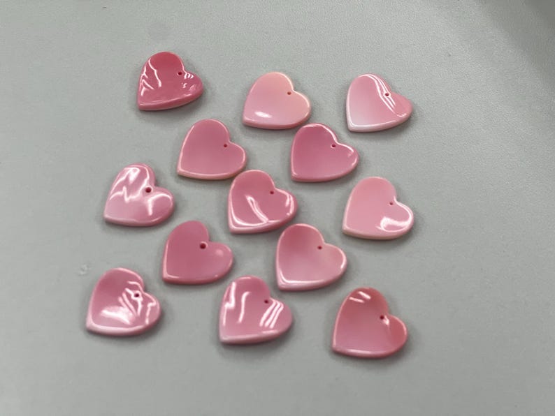Puede incluir: Una colecci&oacute;n de cuentas de concha de coraz&oacute;n rosa. Las cuentas son de diferentes tama&ntilde;os y tienen un ligero brillo iridiscente.
