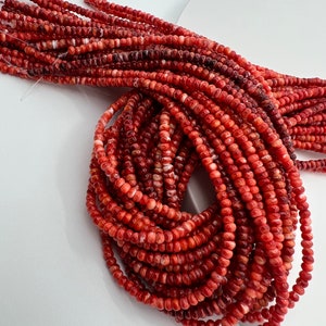 Puede incluir: Una hebra de cuentas de coral rojo y blanco. Las cuentas son pequeñas y redondas, y están enhebradas en un hilo transparente.